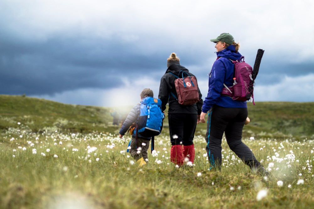 To kvinner og et barn går gjennom en myr med fiskeutstyr