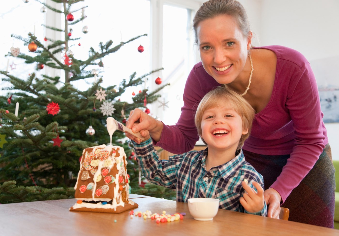 Mor og sønn pynter et lite pepperkakehus